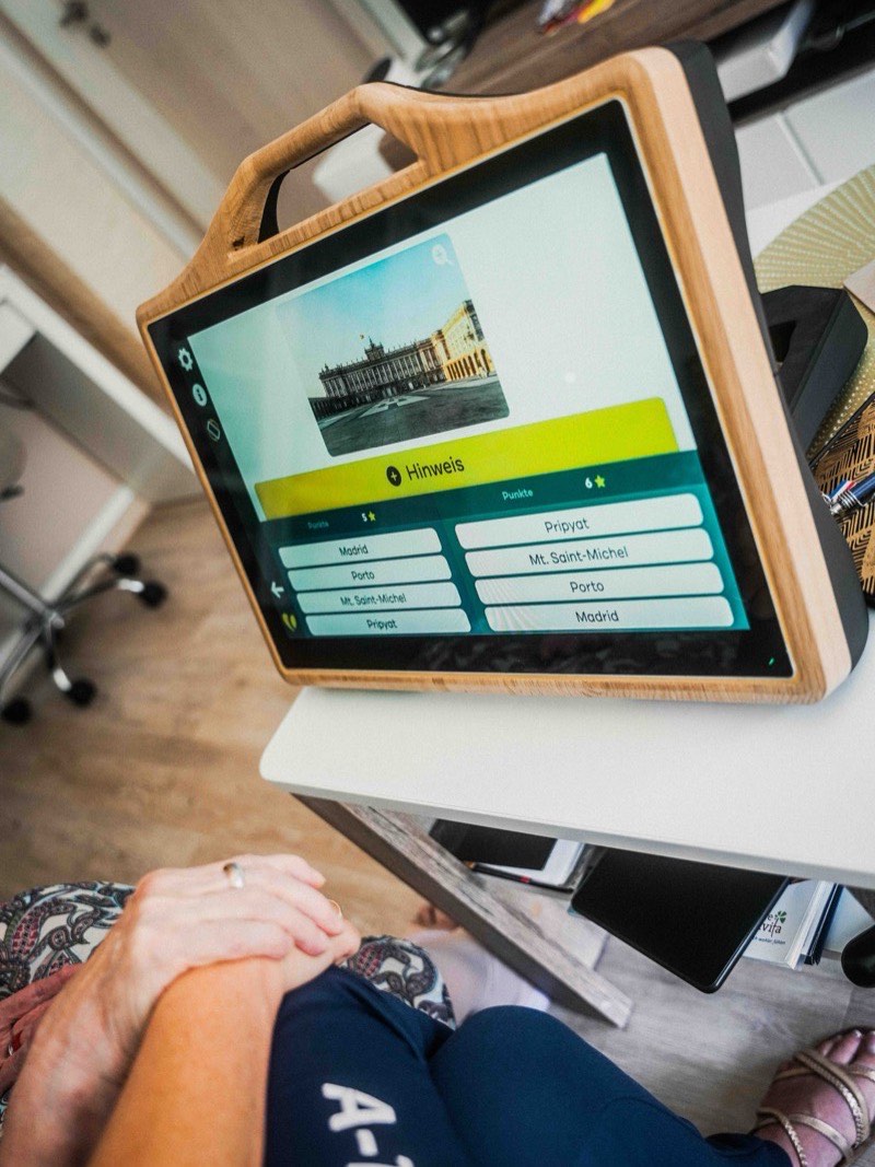 CareTable Mini mit Quiz-App auf einem kleinen Tisch, davor sitzt eine Person