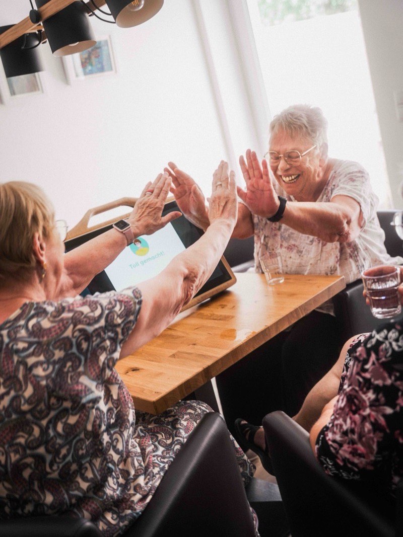 Zwei Seniorinnen klatschen sich über dem CareTable Mini ab